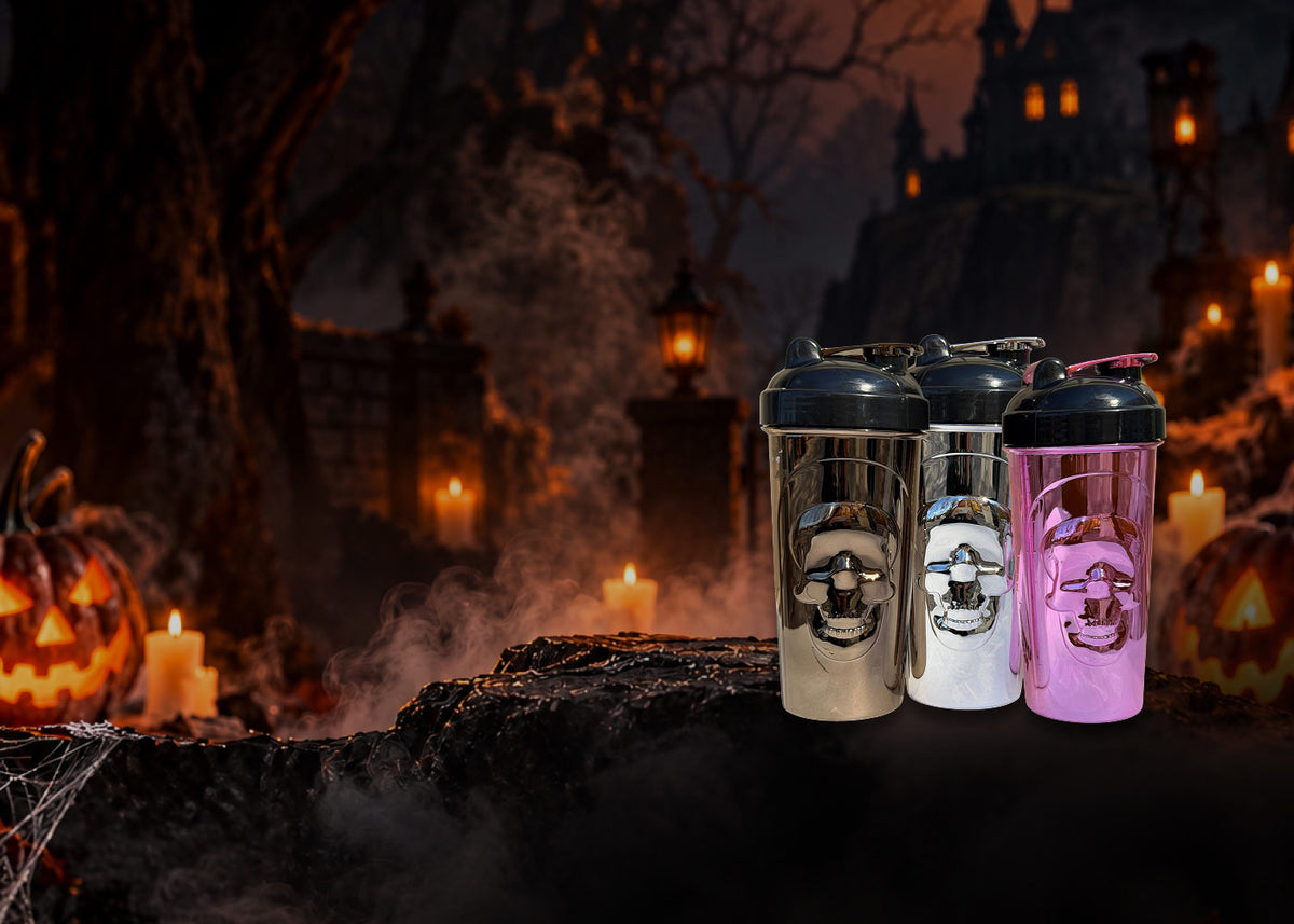 Three shaker bottles with skull graphics in silver, white, and pink, set against a spooky Halloween night background with pumpkins, candles, and a haunted house.